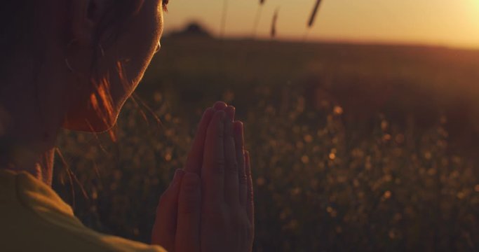 Close up shot of female hands joined in praying gesture on nature sunset background slow motion. Spiritual woman joining palms Namaste in golden evening light outdoors. Body spirit mind concept