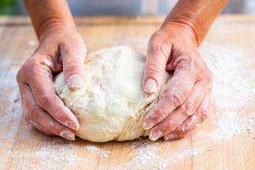 Woman hands kneading dough on the wooden board.