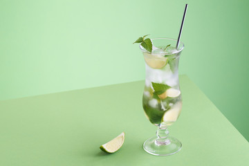 Minimalistic mojito cocktail on a green background with lime piece and silver straw. Photo with place for your text.
