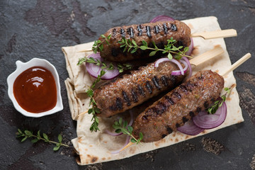 Grilled beef kabobs with lavash flatbread and dipping sauce, studio shot on a brown stone surface, selective focus