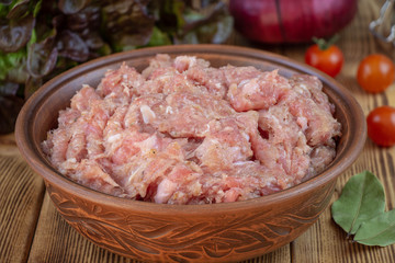 Raw minced pork in a plate and fresh vegetables on a table close-up.