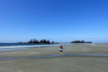 Fototapeta na wymiar A young female tourist enjoying her view of the coast and ocean walking along Chesterman Beach outside of Tofino, British Columbia, Canada. 