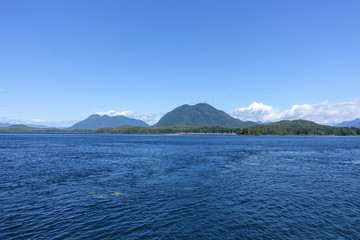 A beautiful vast full view blue seascape ocean photo with forested mountains in the background on a beautiful summer day in a tofino