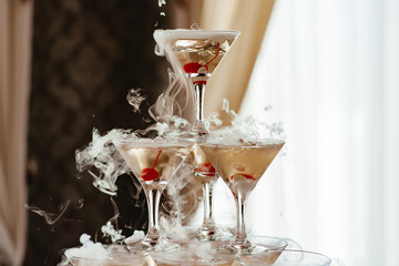 Champagne slide. Pyramid or fountain made of champagne glasses with cherry and steam from dry ice