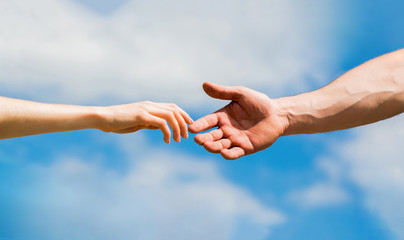 Hands of man and woman on blue sky background. Lending a helping hand. Solidarity, compassion, and charity, rescue. Hands of man and woman reaching to each other, support. Giving a helping hand