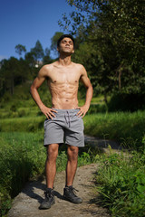 Young handsome shredded boy standing shirtless on the pathway. Fitness and health.