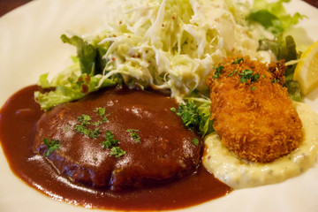 たっぷりのデミグラスソースとパセリのみじん切りのかかった、メダル型のハンバーグステーキと俵型の、ベシャメルソースとシーフードのクリームコロッケとタルタルソース、キャベツの千切りのサラダ。