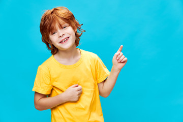 child with red hair on a blue background points up and laughs Copy Space