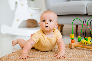 Cute toddler in yellow bodysuit sits at home on the floor playing in a developing toy. child development concept