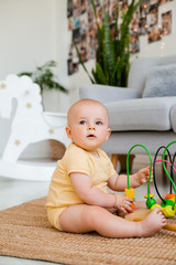 Cute toddler in yellow bodysuit sits at home on the floor playing in a developing toy. child...