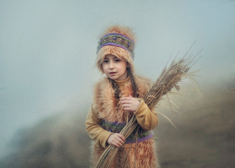 A girl in a fur hat and coat with a bouquet of dried grass in the fog.