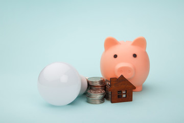 Piggy bank with money banknote and led light bulb, house figure on blue background. Power saving concept.