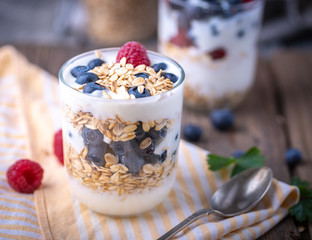 White yogurt in glass jar with fruits on yellow napkin.