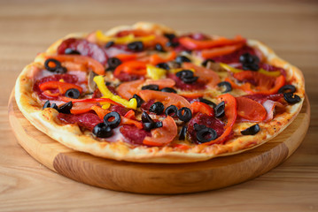 Fresh pizza with tomatoes, cheese and mushrooms on wooden board over rustic wooden table background closeup.
