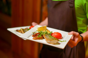 Fish dish - fried fish fillet with vegetables served on a white plate. Restaurant service, eating out in a restaurant.