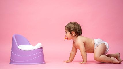 Cute baby in a diaper crawls to the potty. Toilet and potty training.