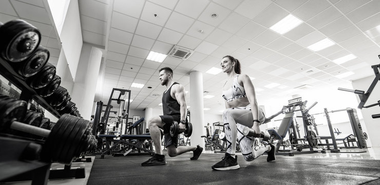 Bodybuilding. Strong fit woman and man exercising with barbells. Muscular blonde girl and strong man are lifting weights in gym. Black and white photo.
