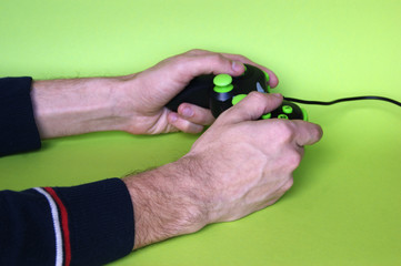 Male hands hold a gamepad in light green background.