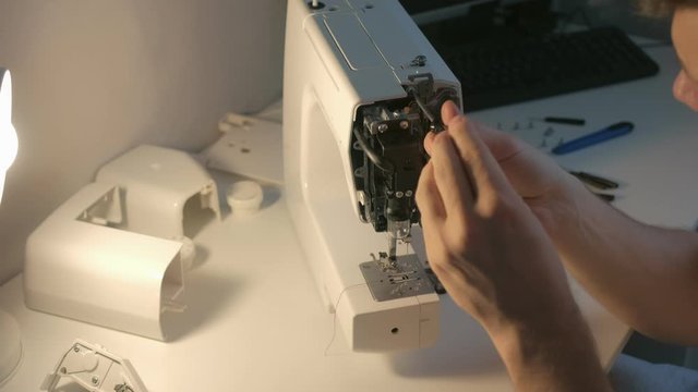 Repairman master is collecting and testing sewing machine after repairing sitting at table in workshop. Maintenance and repair of sewing machine and home appliances. Screwing the bolt screwdriver.