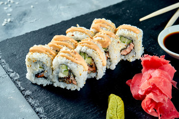 Sushi roll california in sesame with avocado, fried salmon, spicy sauce and philadelphia cheese on a black slate board. Selective focus