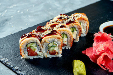 Sushi roll golden dragon with eel, salmon, philadelphia cheese and unagi sauce on a black slate board. Selective focus