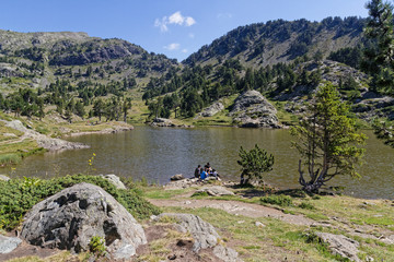 CHAMROUSSE, FRANCE, July 25, 2020 : A group of hikers rest for a while on the shore of a beautiful mountain lake near the summer resort.