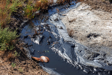 Spilled streams of liquid crude oil flow down drainage ditch into public body of water. Environmental disaster Oil pollution of environment from obsolete technologies and ancient production equipment