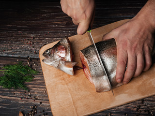 man cuts a trout with a knife on a Board. Fresh raw fish