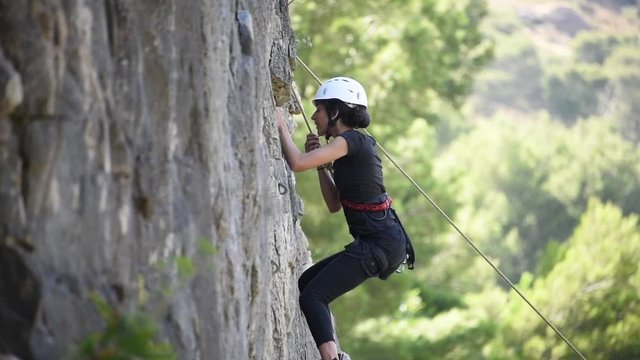 Healthy fit girl rock climbing rapels down steep stone wall on rope