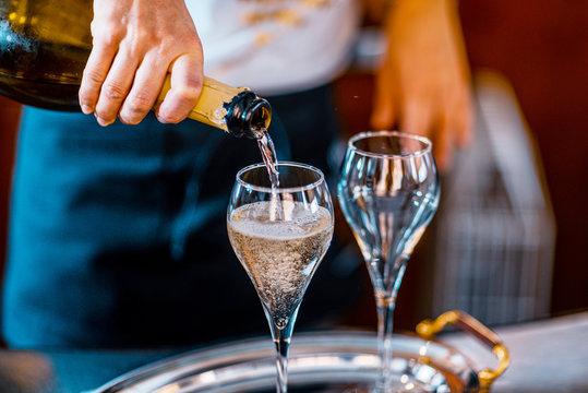 Female barista sommelier hand in a bar pouring sparkling white wine as prosecco millimesimato, champagne on dessert glasses for toast celebration