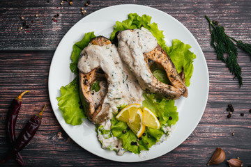 fried red fish in cream sauce with lemon and lettuce in white plate
