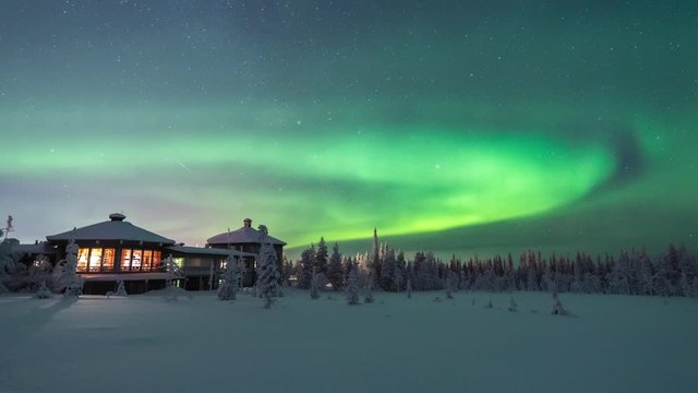 Timelapse of green northern lights in the starry night sky above a old wooden building covered with snow in Yllas, Lapland Finland.