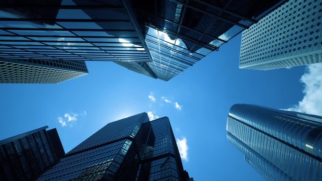 Time lapse of low angle view of city skyline buildings, blue sky and glass mirrored facades.	