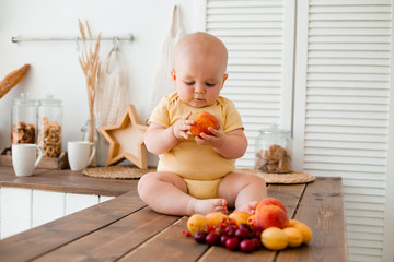 Cute toddler eats fruit in wooden kitchen at home