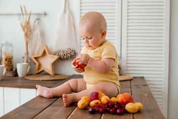 Cute toddler eats fruit in wooden kitchen at home