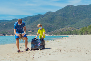 Volunteers blue face mask paradise beach sand lazur sea. Father son pick up garbage into black bag....