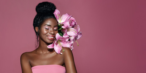 Fashion portrait of young African American model with pink art make up posing with lily flowers...