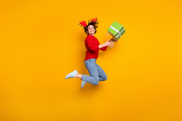 Full size profile photo of pretty funny lady jump high up catch low price surprise gift box rejoice wear headband x-mas horns red knitted sweater jeans shoes isolated yellow color background