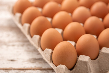 Many fresh raw brown chicken eggs in carton box on white rustic vintage wooden kitchen table background.