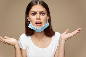 Upset woman with a medical mask on her ears spreads her hands to the sides