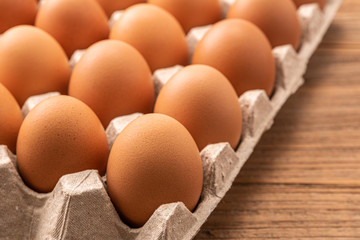 Many fresh raw brown chicken eggs in carton box on rustic vintage wooden kitchen table background.