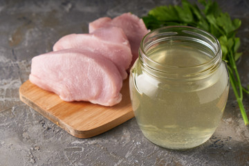 fresh poultry broth in a glass jar on a table with vegetables and pieces of fresh poultry meat