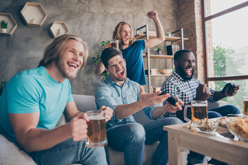 Portrait of four nice attractive cheerful cheery ecstatic guys playing video game sport battle contest having fun spending weekend at industrial loft style interior house apartment flat indoors