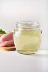 fresh poultry broth in a glass jar on a table with vegetables and pieces of fresh poultry meat