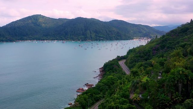 Aerial: drone shot in brazil santa rita beach  ubatuba with view to yacht park sailboats in ubatuba on the road that passes near the sea and the jungle during sunset sao paulo san pablo litoral north