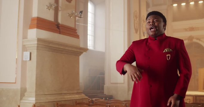 Afro american male gospel singer in 30s. Young man wearing red suit moving hands while singing spiritual music in house of prayer. Concept of religion and people