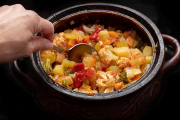 Close-up of a hand mixes vegetable stew in a saucepan with a spoon. Healthy food concept. Vegetarian food concept
