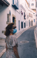 Beautiful curly brunette tourist with a surgical mask during Covid-19 in the Mediterranean village of Sitges, Barcelona province. Safe Travel in the new normal concept