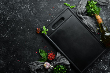 Kitchen board with spices and herbs on a black stone background. Top view. Free space for your text.