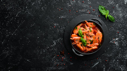 Food. Boiled shrimp in tomato sauce with basil on a black stone plate. Top view. Free space for your text.